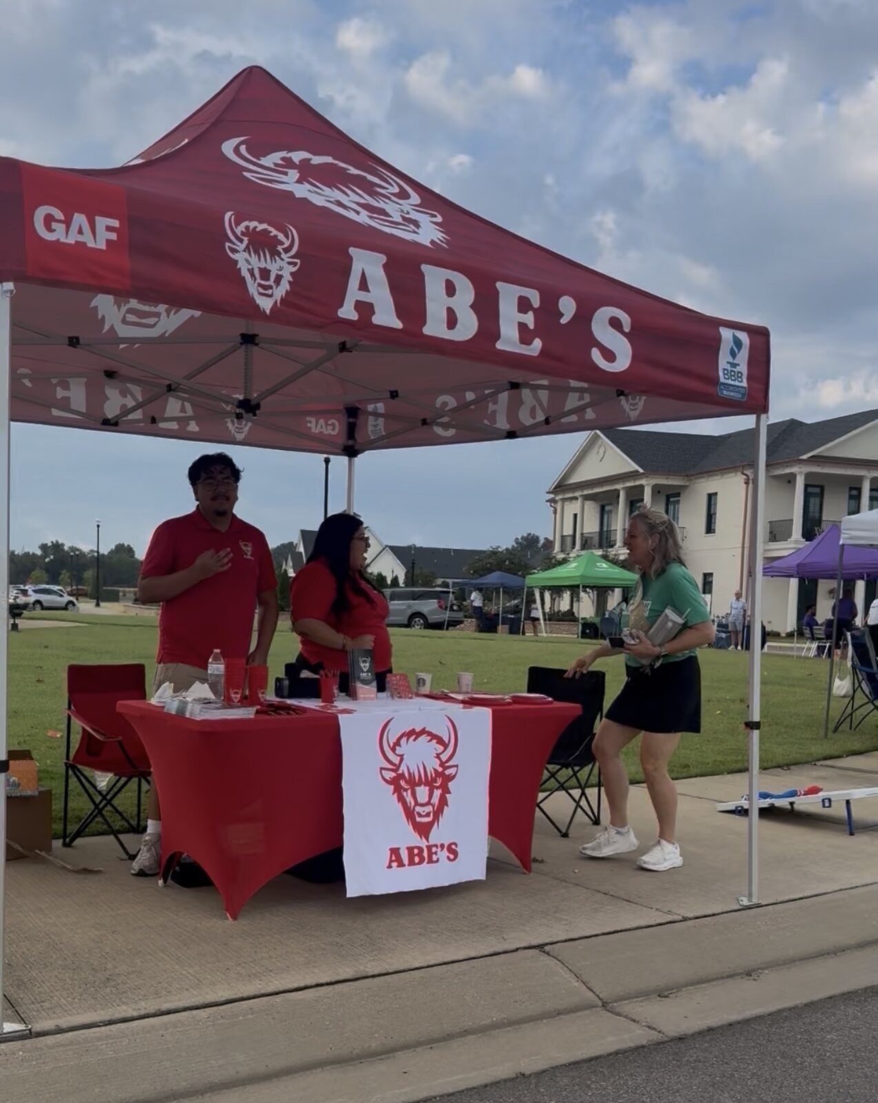 People talking at Abe's booth under a red canopy at the 5K