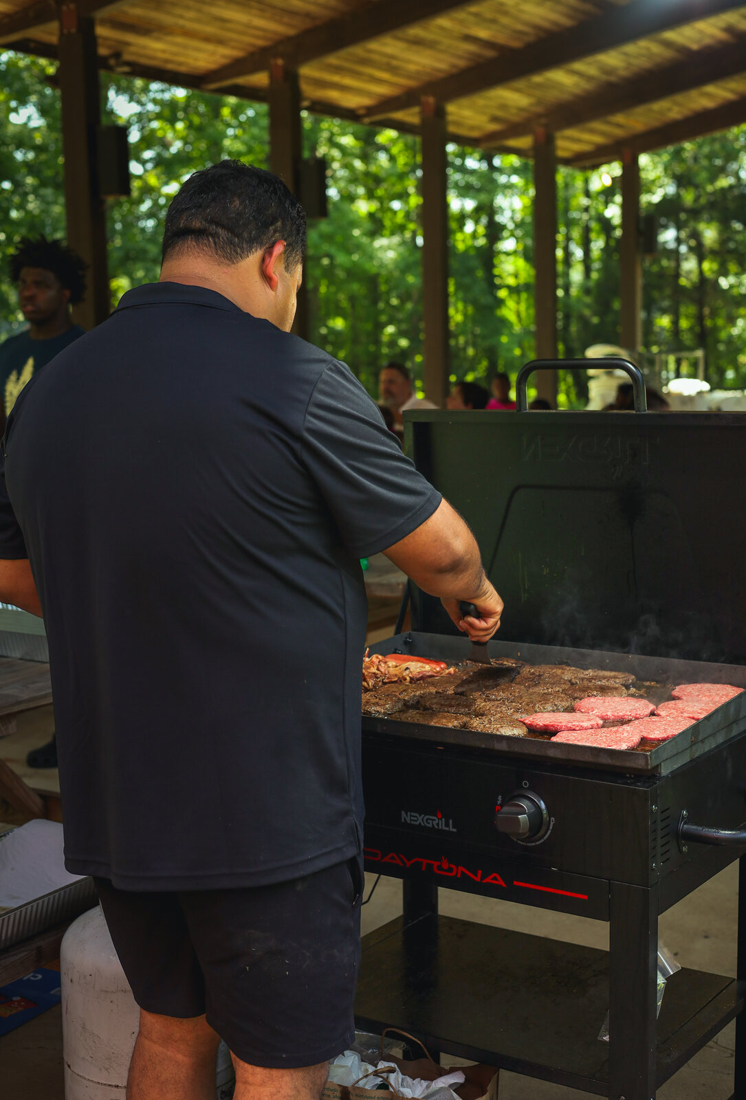 A person cooking burgers on an outdoor grill at the event